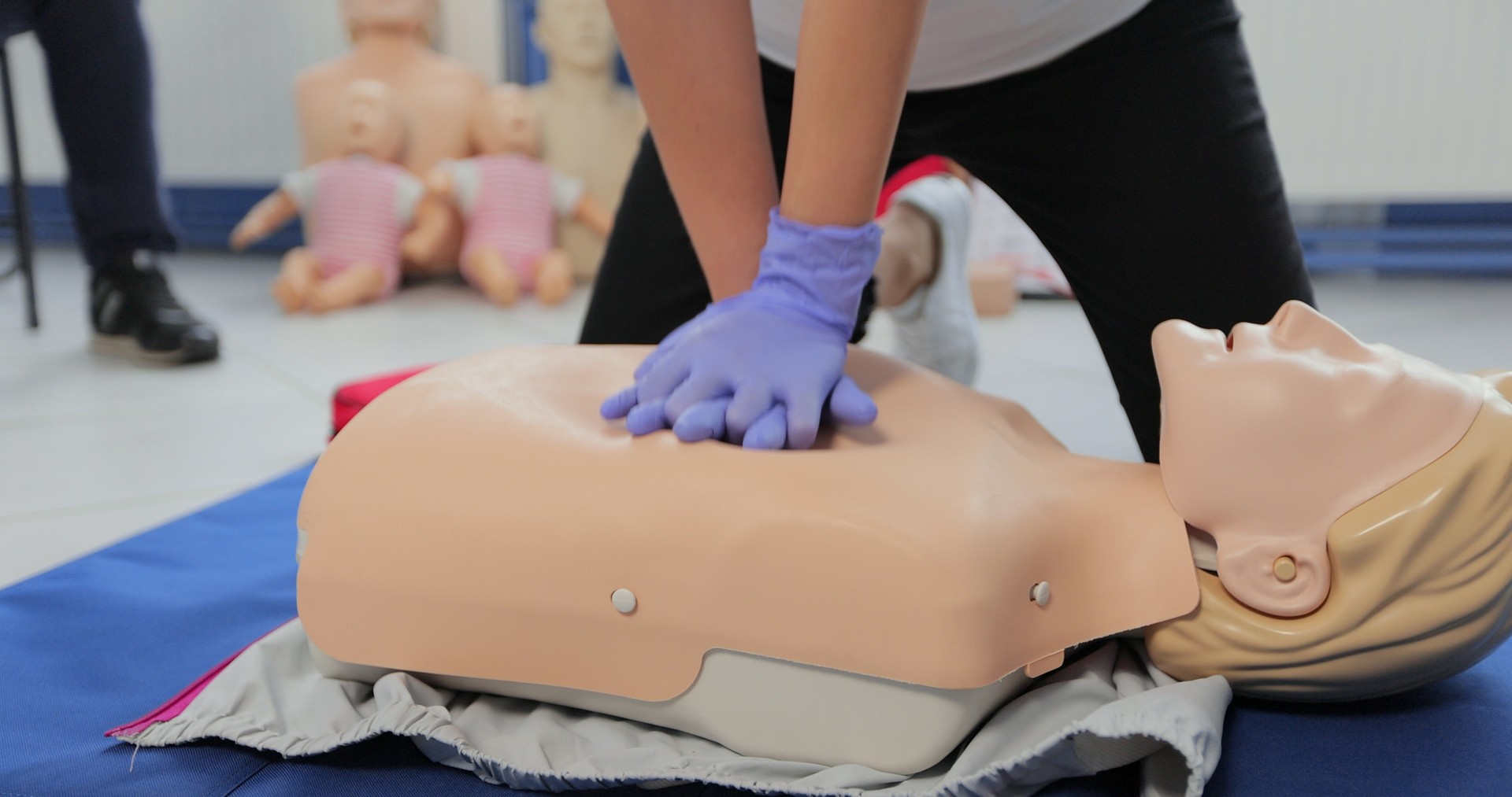 Woman demonstrating CPR on mannequin in first aid class.